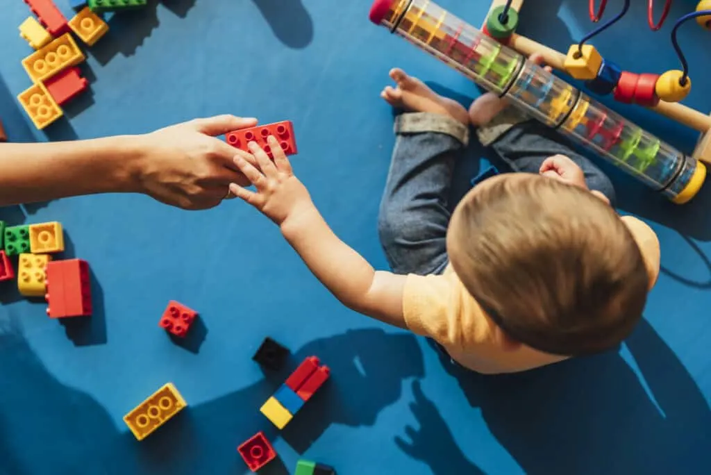 Photograph of a baby reaching for a toy  block that they are being handed.