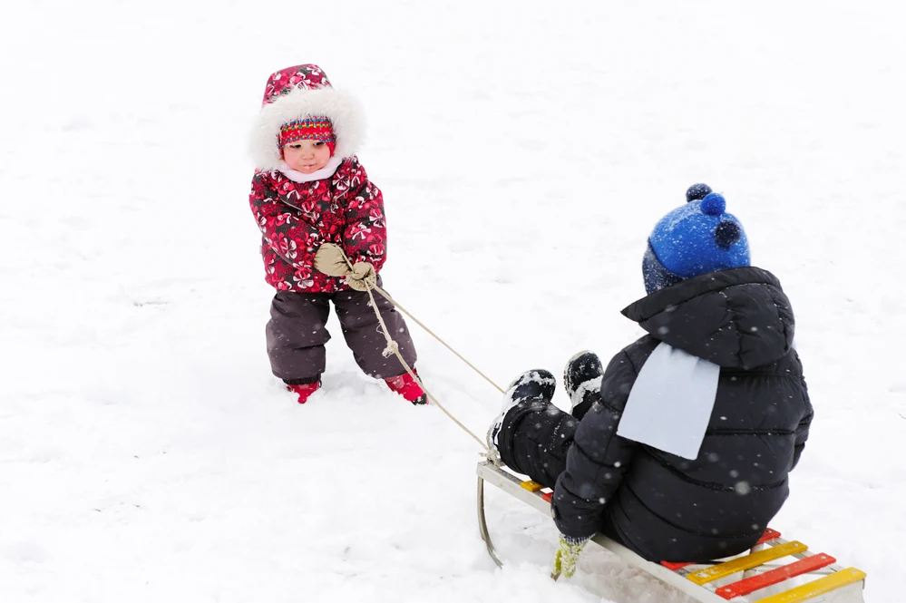 Image of one child pulling another child in the snow on a sled.