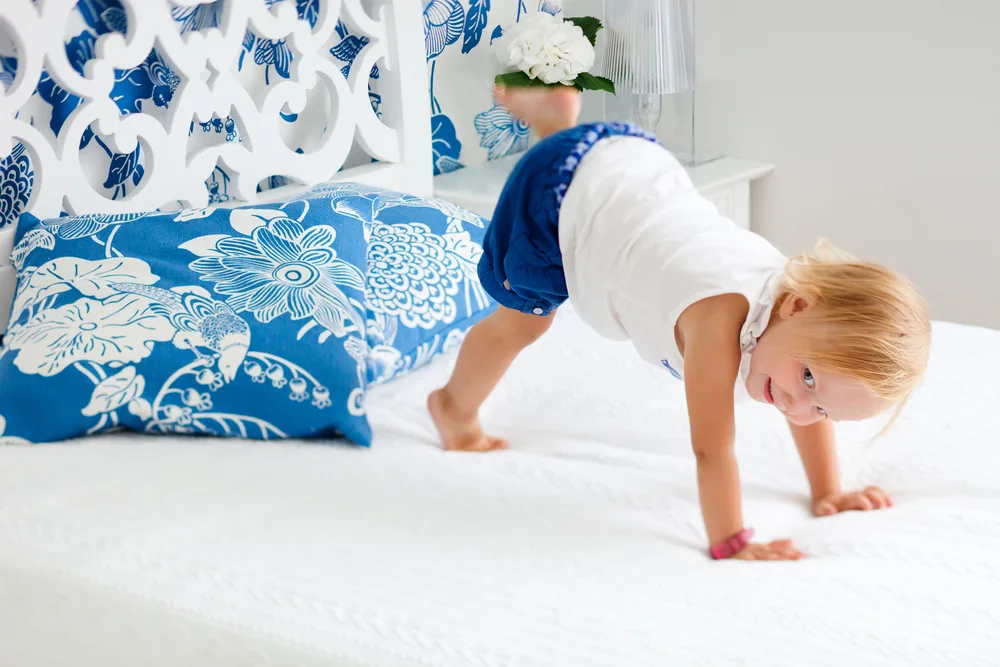 Toddler using gross motor skills to balance on bed