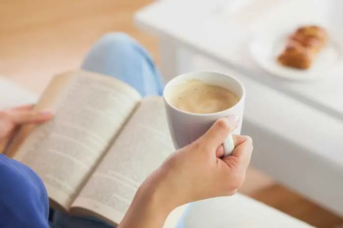 person holding a cup of coffee while reading a book