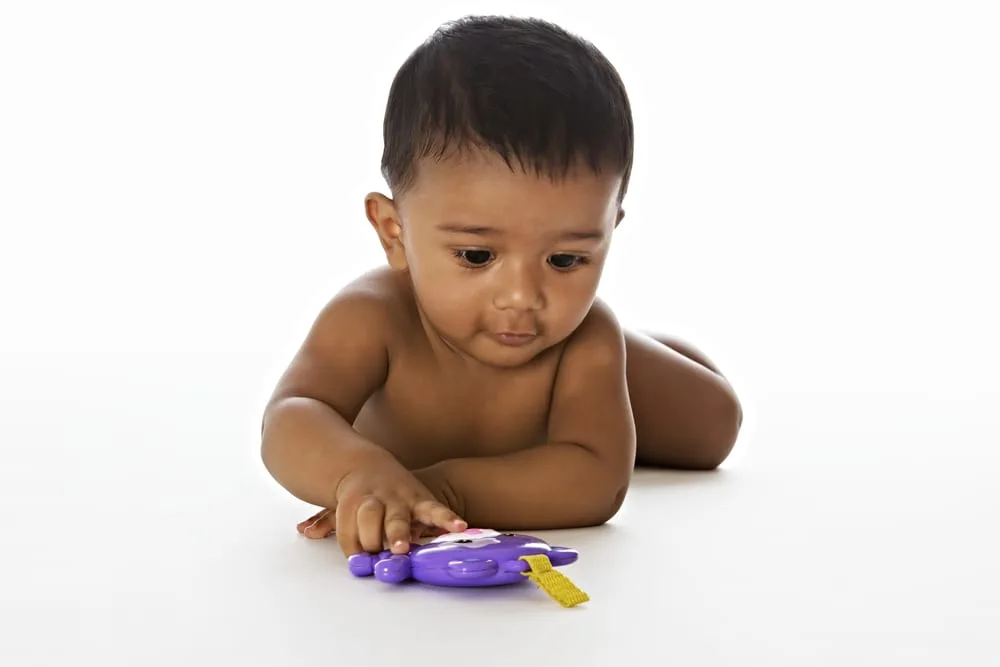 Adorable Indian baby lying on floor and playing with a toy, isolated on white background.