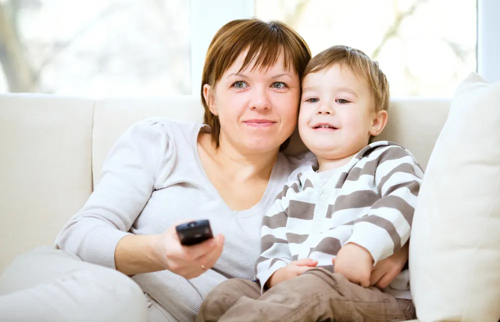 Mother and her son are watching tv while sitting on a couch